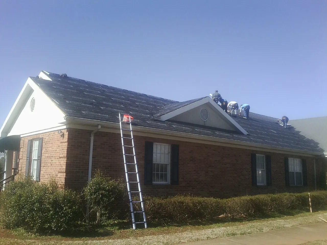 Crew tearing shingles off a brick ranch roof with a ladder set — Metal Roof Repair work by our crew in Fremont Center