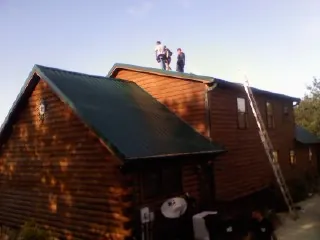 Crew on the ridge of a green metal roof on a two story log home in Fremont Center