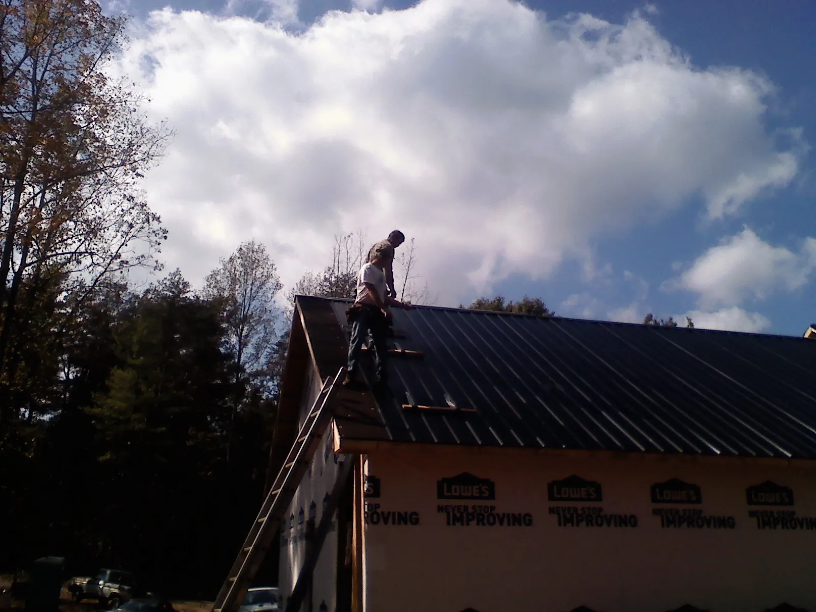 Roofer fastening dark metal panels high against a cloudy sky, from a Roof Inspection job in Fremont Center