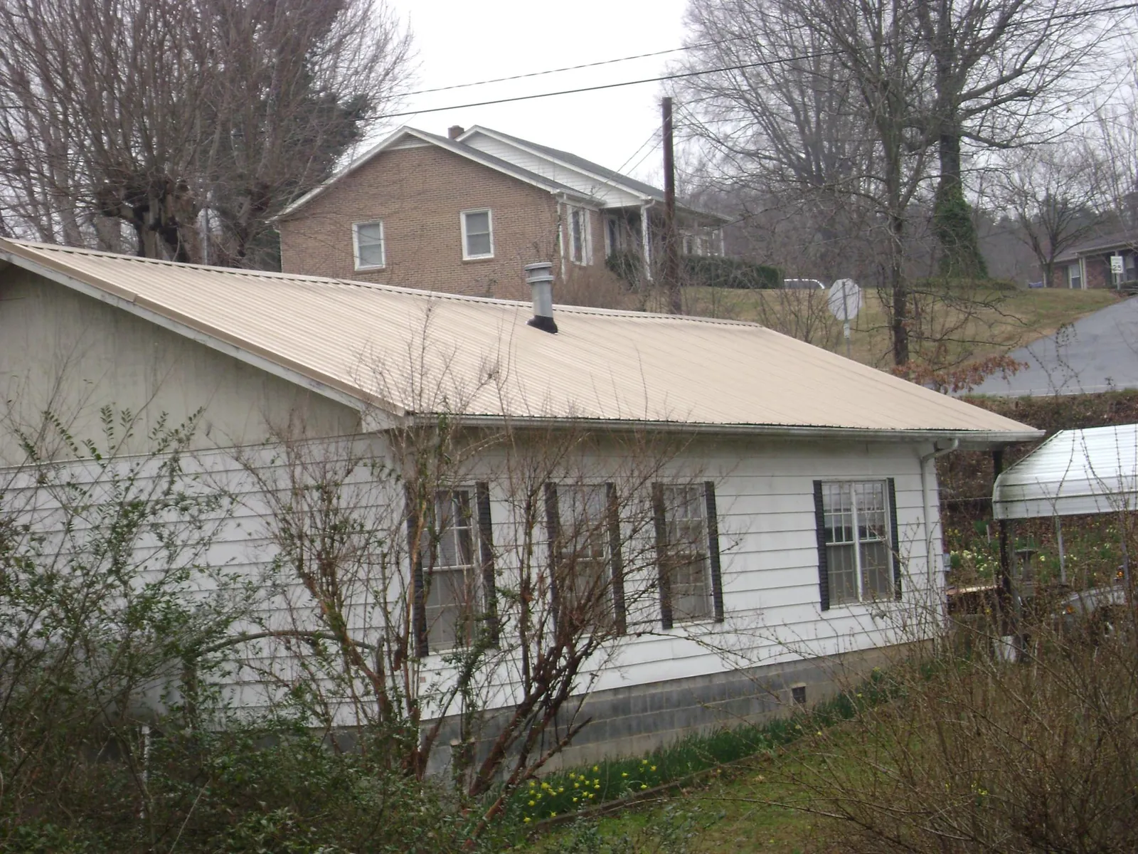 Tan metal roof on a white sided house set into a hillside — Commercial Roofing by Roofing Brothers in Fremont Center